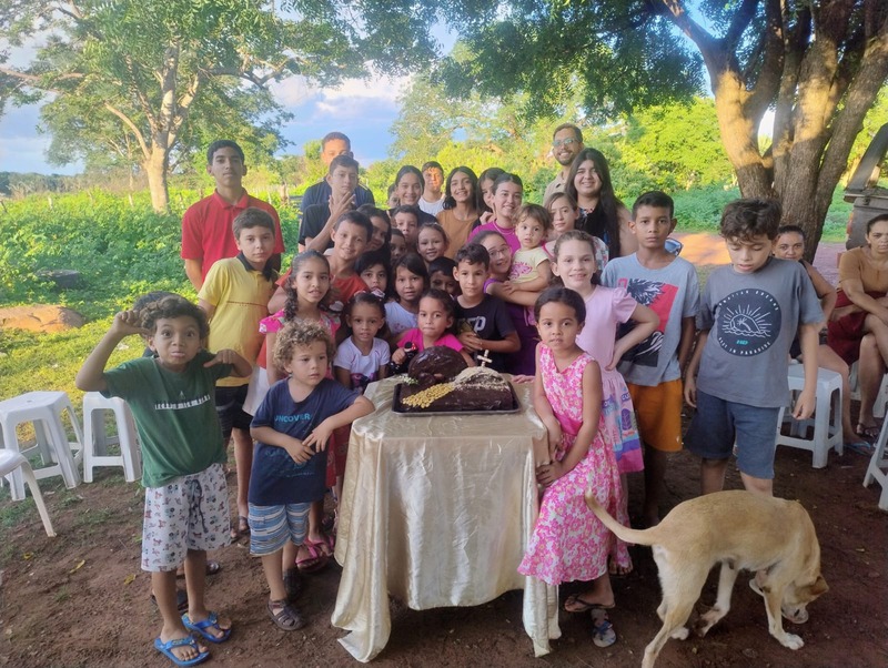 Grande grupo de crianças reunidas ao ar livre em torno de um bolo