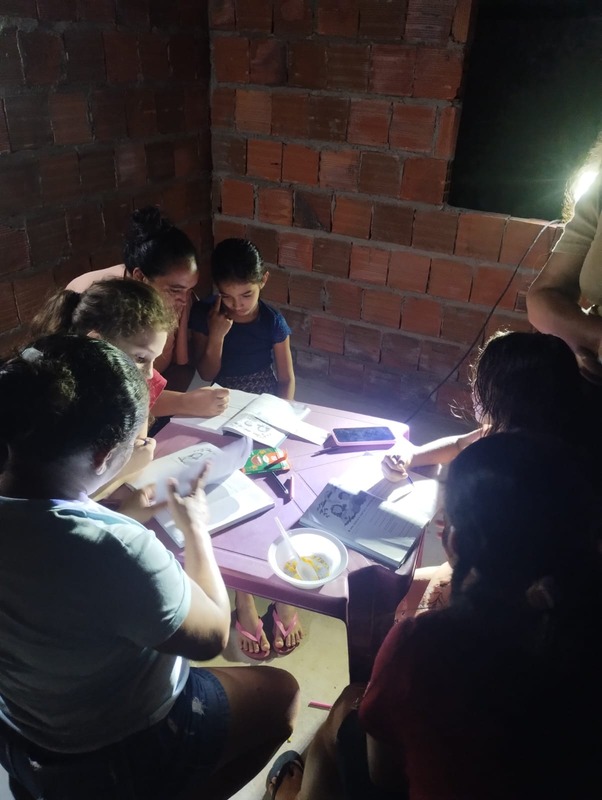 Família reunida ao redor da mesa em estudo bíblico noturno numa casa de tijolos