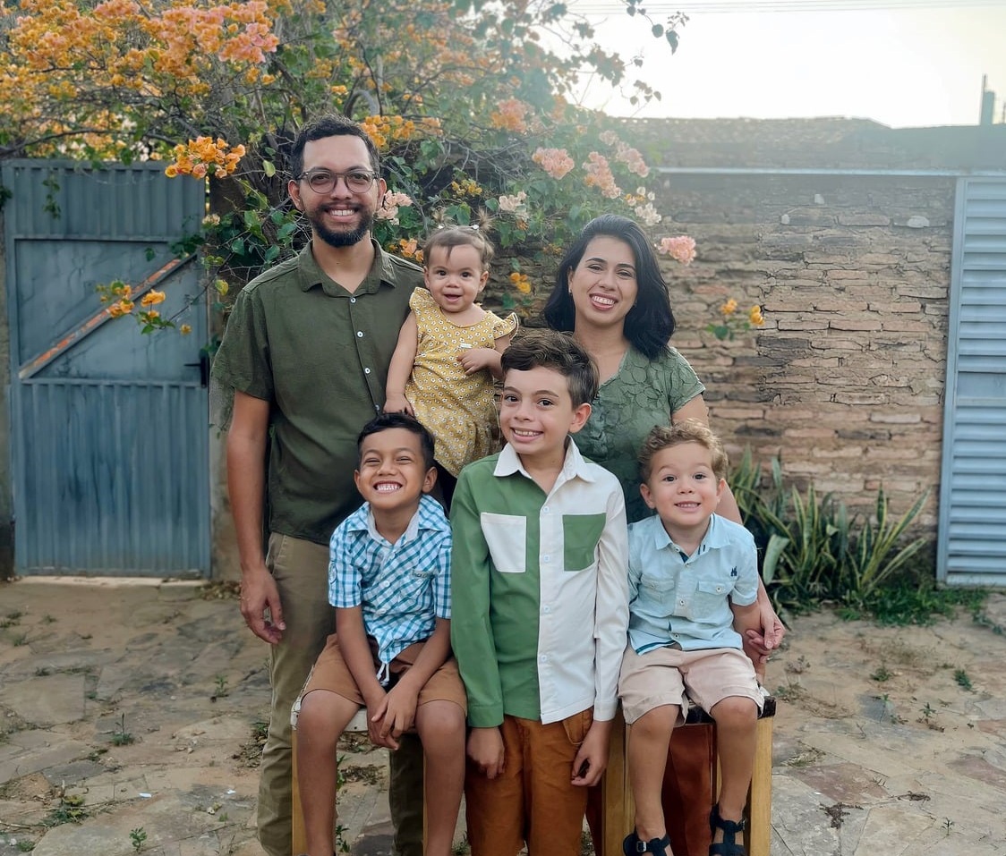 A Família Ramos ao entardecer no sertão, diante de um muro de tijolos e buganvílias floridas